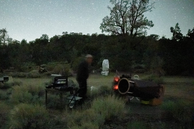 Man walking to a telescope in the dark in a mountainous landscape