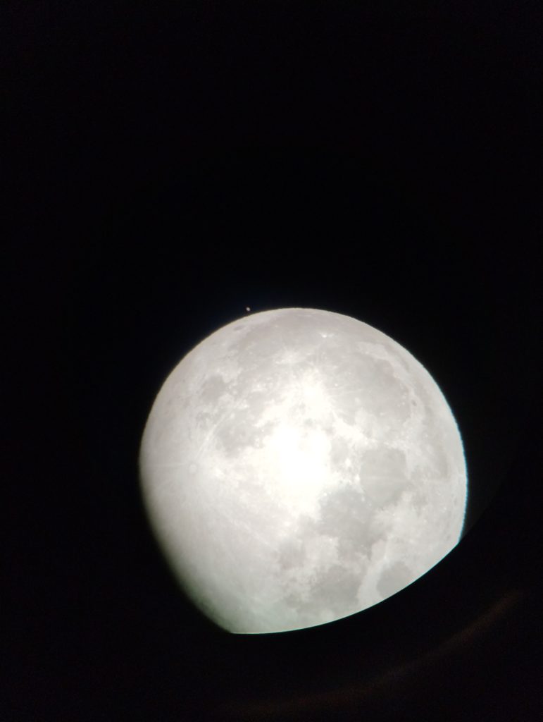 A picture of the moon with a Mars as a tiny dot near the top of the moon. The lower half of the moon is cut off by the telescope tube.